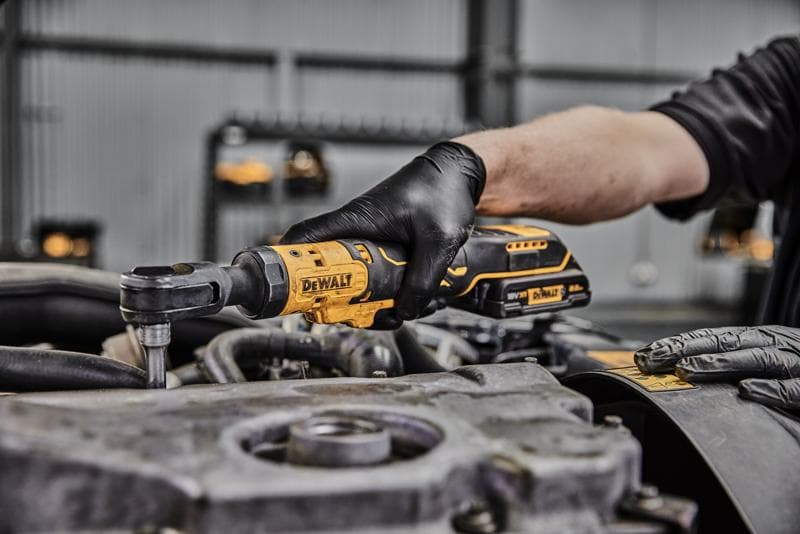 Uma pessoa usando luvas pretas utiliza uma ferramenta de catraca sem fio DEWALT em um componente de motor em uma oficina.