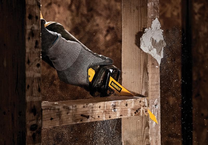Close de uma mão usando uma luva cinza operando uma serra sabre DEWALT para cortar uma viga de madeira, com serragem sendo espalhada no ar.
