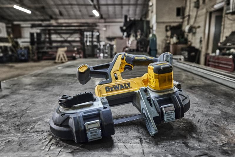 DEWALT cordless band saw on a workshop table, industrial setting in the background.