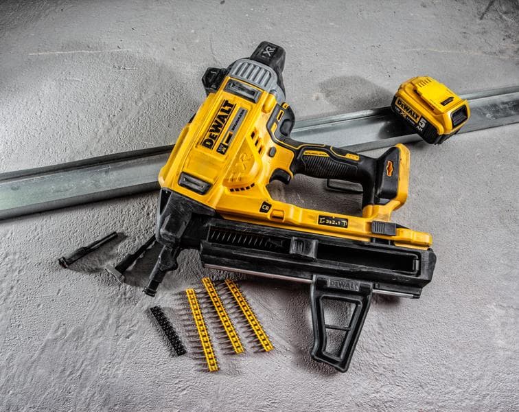 Uma pistola de pregos sem fio DEWALT com bateria, várias tiras de pregos e acessórios sobre uma superfície de concreto. A ferramenta é predominantemente amarela e preta e projetada para trabalhos de construção pesada.