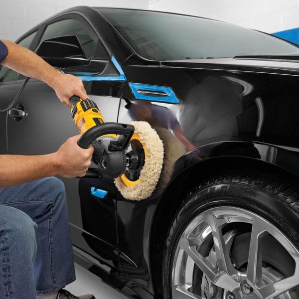 Uma pessoa utiliza uma polidora DEWALT DWP849X para polir o lado de um carro preto, com fita azul aplicada em algumas áreas para proteção.