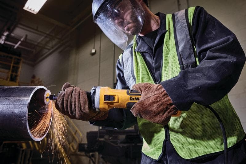 Uma pessoa vestindo equipamentos de segurança usa uma ferramenta elétrica DEWALT para cortar ou lixar um tubo de metal, produzindo faíscas.