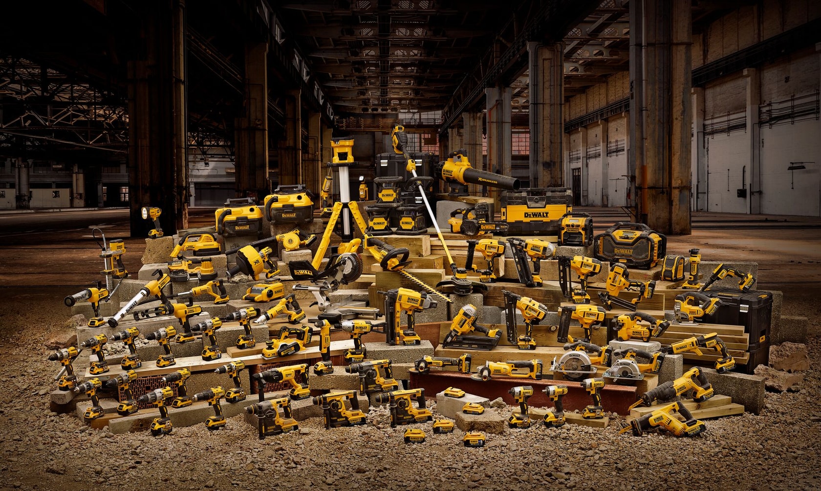 Uma grande variedade de ferramentas elétricas e acessórios DEWALT, incluindo furadeiras, serras, esmerilhadeiras e caixas de ferramentas, está disposta em blocos de concreto em um ambiente de armazém industrial.