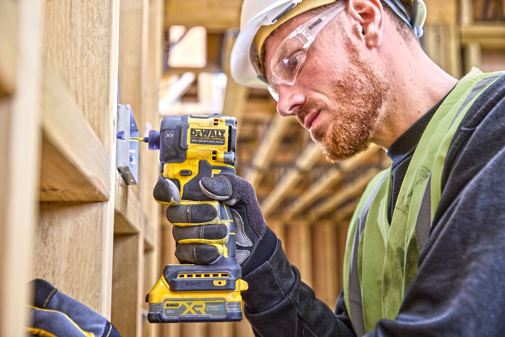A worker using a DEWALT DCF870NT cordless impact wrench to secure a metal bracket onto wooden beams at a construction site